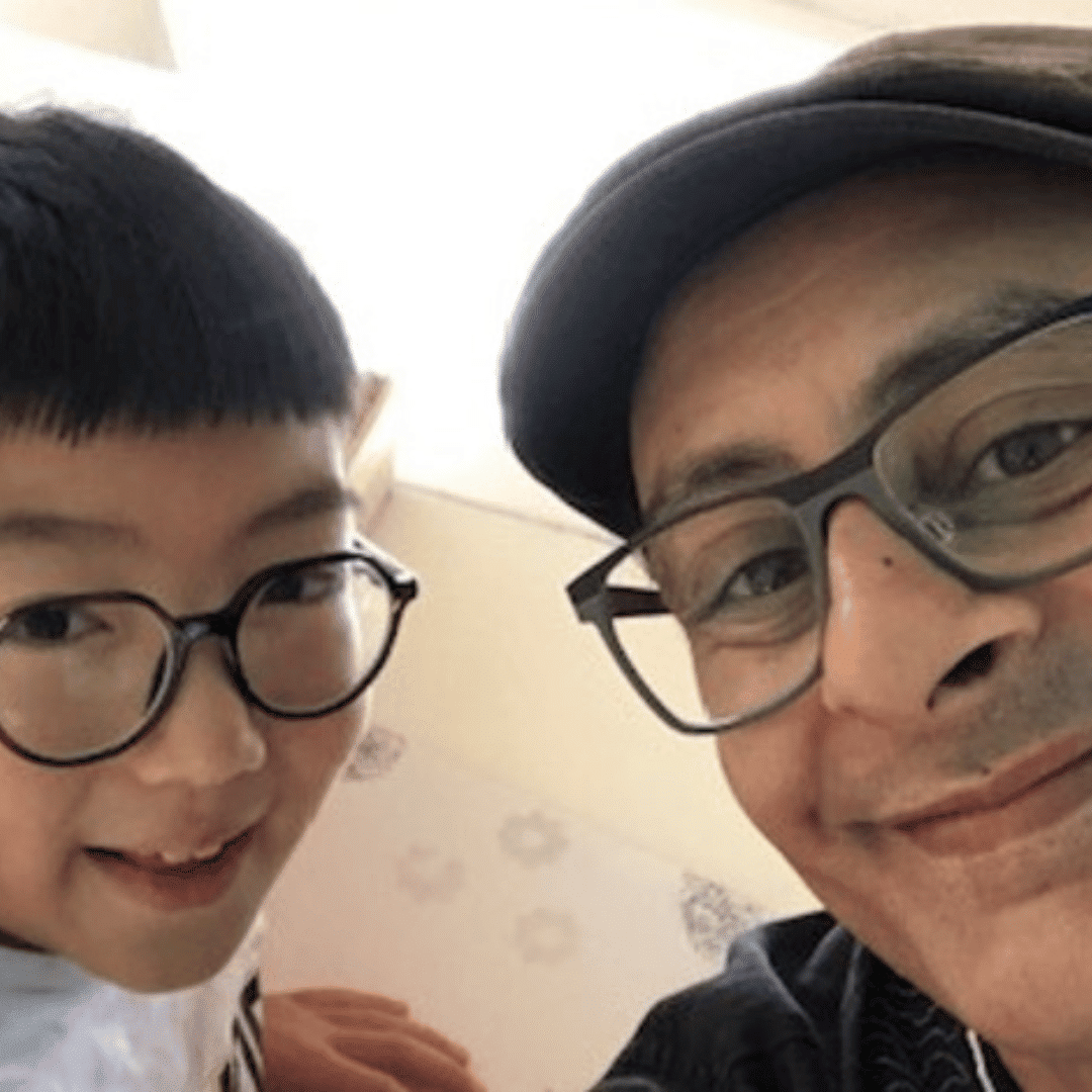 Chines boy with glasses and indian man wearing a hat and glasses smiling at the camera