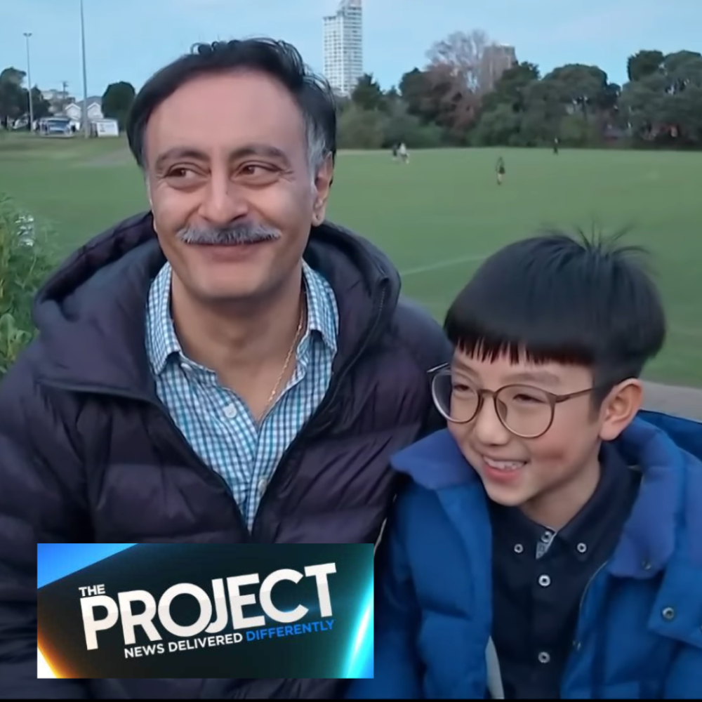 Man and boy together looking happy with sports field behind them. Logo of The Project is showing
