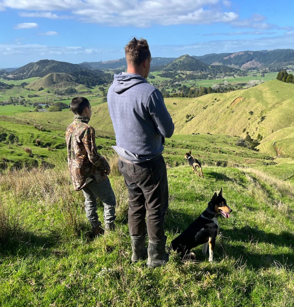 A man and a boy look out across the hills with a dog by their side